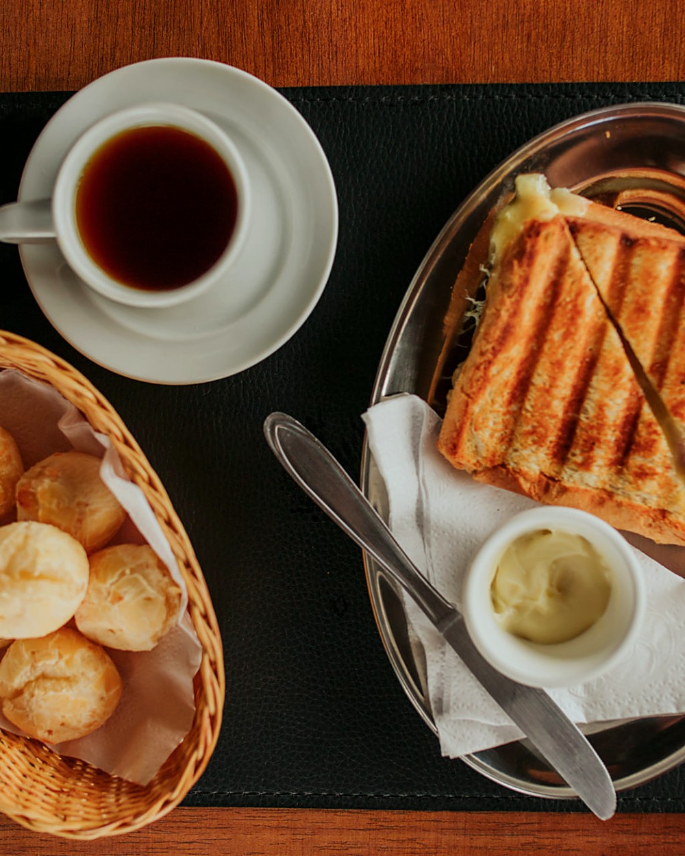 Café coado, pães de queijo e sanduíche tostado servidos sobre mesa de madeira