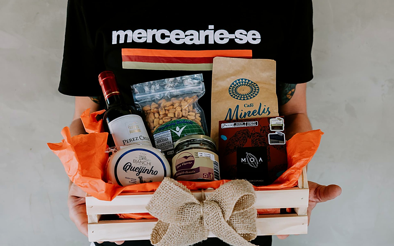 Cesta de presente com vinho, café, queijo, chocolate e laço de juta